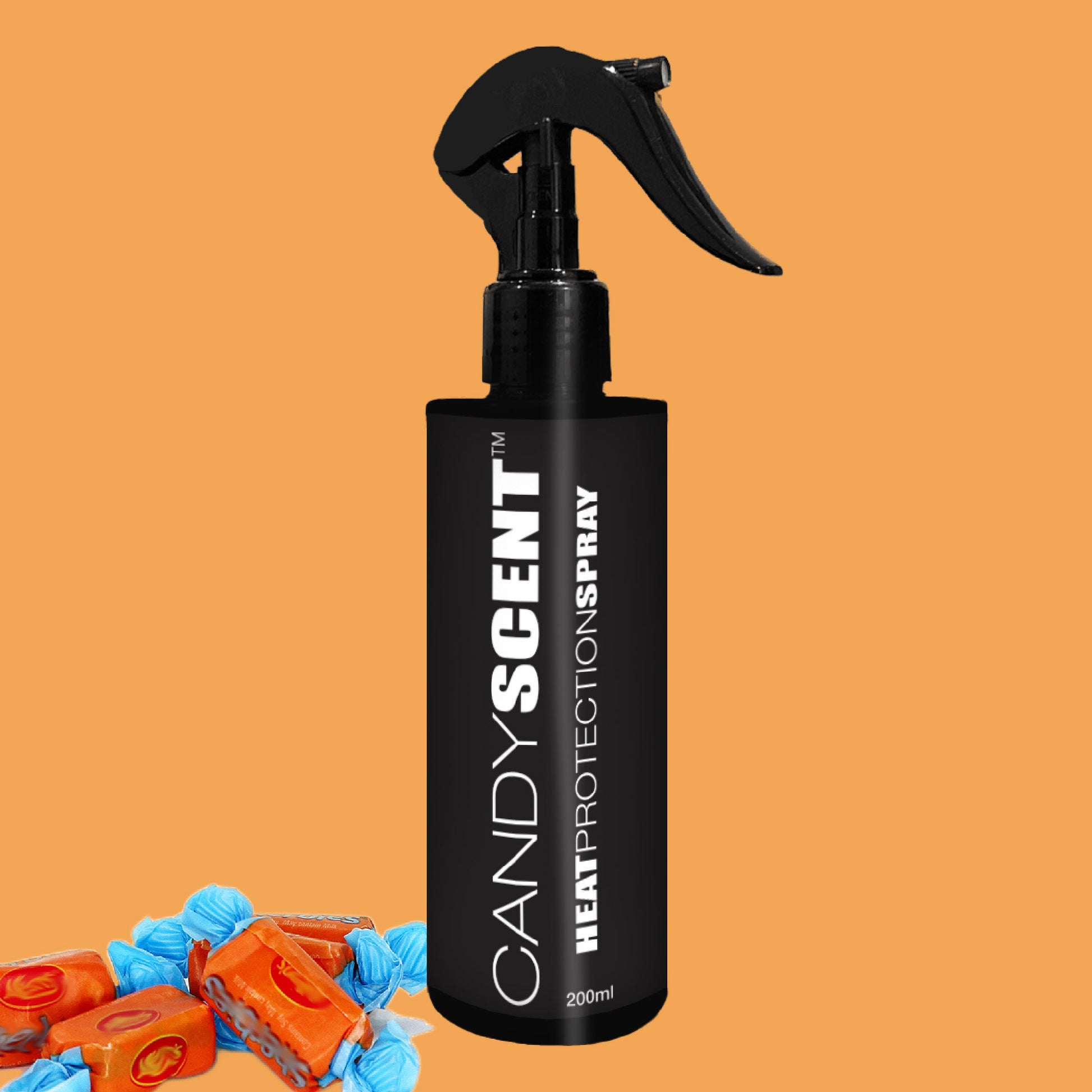 A black CANDYSCENT™ Heat Protection Spray bottle is placed against an orange backdrop, with wrapped blue and caramel candies nestled in the lower left corner.