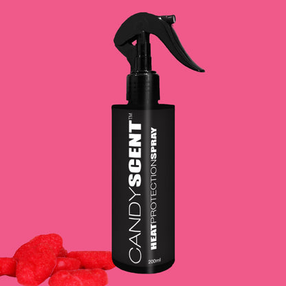 A black spray bottle labeled "Heat Protection Spray" by CANDYSCENT™, featuring a trigger nozzle, is set against a pink background, ideal for achieving salon-quality hair. The CANDYSCENT™ fragrance fills the air, with red candy pieces creatively scattered in the lower left corner.