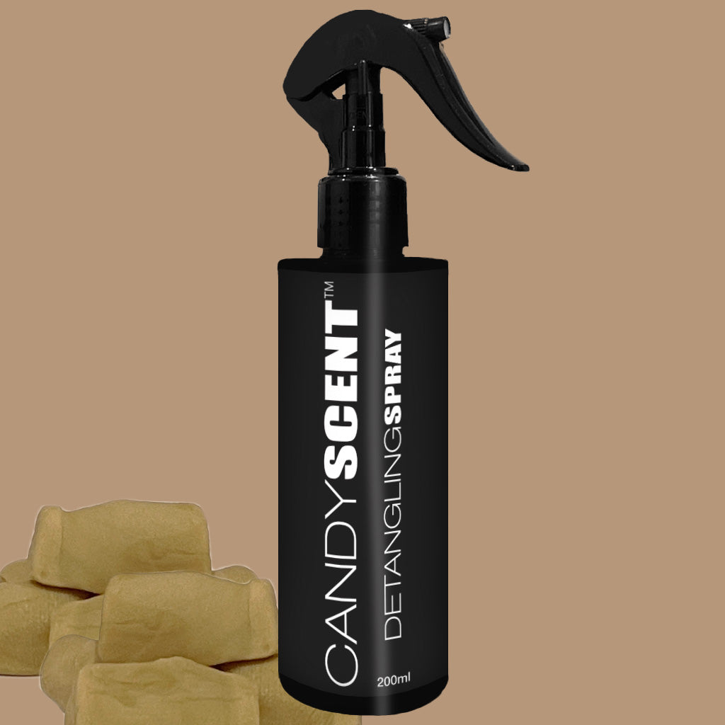 A black bottle of CANDYSCENT™ Hair Detangling Spray, featuring a spray nozzle and enriched with jojoba oil, is labeled "200ml" and placed against a beige background. Three caramel-colored candies are positioned to the left of the bottle.