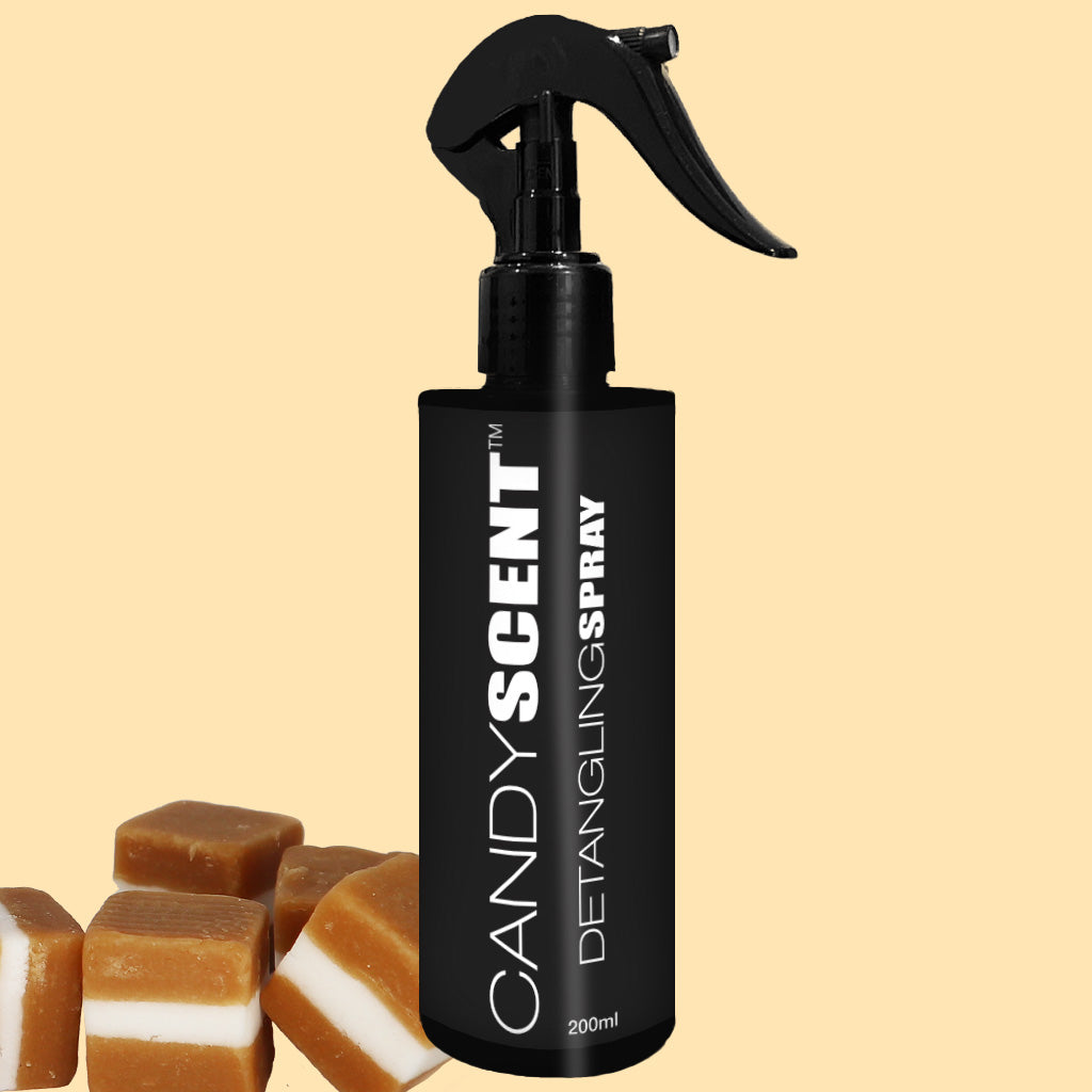 A black bottle of CANDYSCENT™ Hair Detangling Spray with a spray nozzle is centered against a light yellow background. The label on the bottle reads "200ml." Infused with jojoba oil and aloe vera, it ensures smooth, tangle-free hair. Several caramel candies are visible in the bottom left corner.