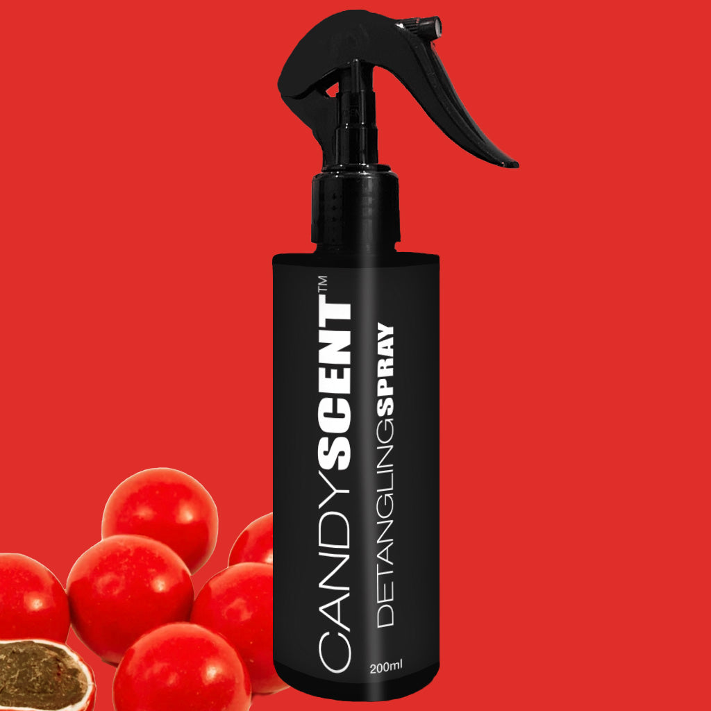 A black bottle of CANDYSCENT™ Hair Detangling Spray with a spray nozzle is showcased against a red backdrop. The bottle features the product name prominently in bold white letters. In the bottom left corner, red berries and a green leaf suggest its nourishing ingredients such as aloe vera and jojoba oil.