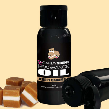 In the foreground is a black bottle labeled "CANDYSCENT™ Fragrance Oil," perfect for your oil burner. The label reads "Jersey Caramel," and nearby, a few pieces of caramel candy with white centers add a sweet touch to your home scent. A second bottle, partially visible, lies on its side on a light beige background.