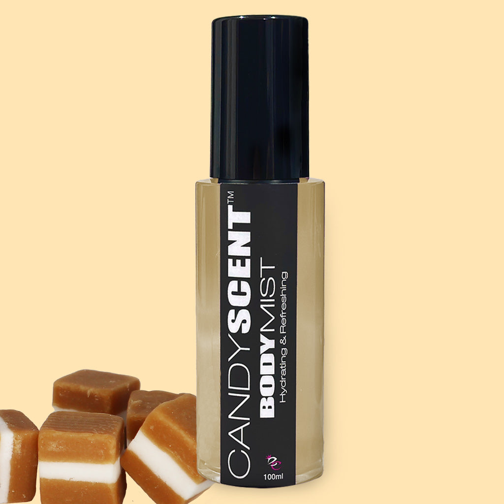 A 100ml bottle of CANDYSCENT™ Hydrating Body Mist with a black cap, enriched with nourishing ingredients like witch hazel, stands against a light yellow background. Several caramel candies are placed near the base of the bottle.