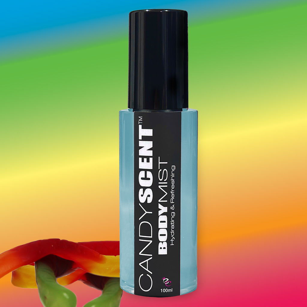 A bottle of CANDYSCENT™ Hydrating Body Mist with a sleek black cap and label stands against a vibrant rainbow-gradient background. The text on the bottle reads "CANDYSCENT™ Body Mist, Hydrating & Refreshing with witch hazel," with a volume indication of 100ml. Colorful gummy candies are visible at the bottom left.