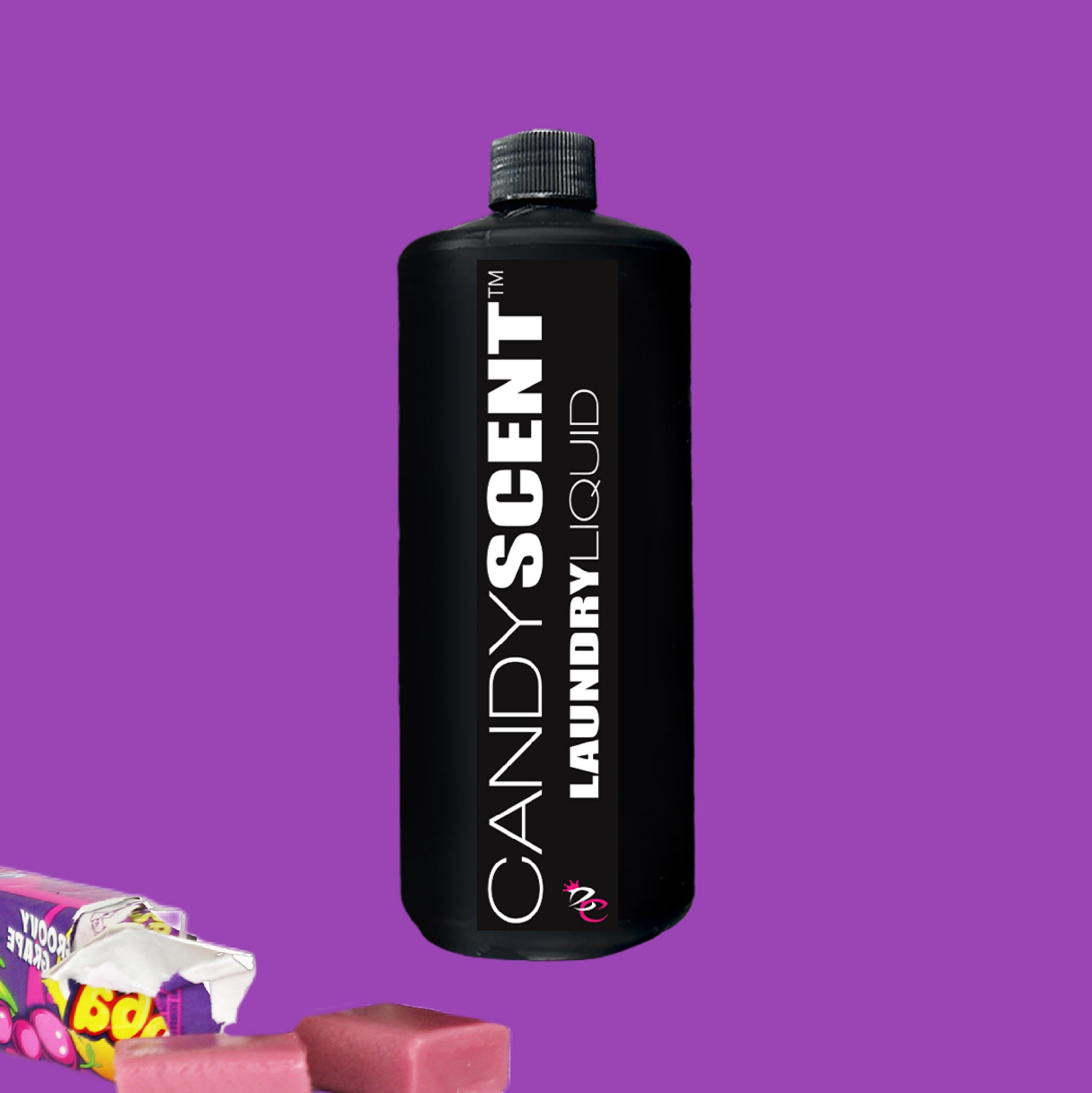 A black bottle labeled "CANDYSCENT™ Laundry Liquid" stands against a purple background, showcasing its eco-friendly formula. In the corner, two pieces of pink candy and a partially visible candy wrapper add a sweet touch to this biodegradable laundry liquid’s presentation.