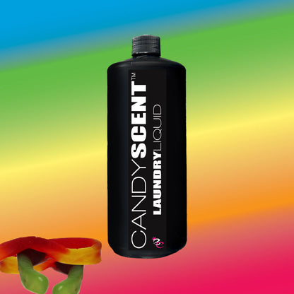 A black bottle labeled "Laundry Liquid" by CANDYSCENT™ stands against a vibrant rainbow gradient background, highlighting its eco-friendly, biodegradable formula. In the bottom left corner, two colorful gummy candy worms add a playful touch.