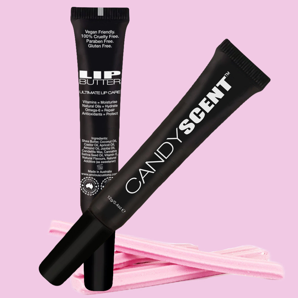 The image displays two black tubes of lip care products against a pink background. One tube is labeled "Lip Butter" from CANDYSCENT™, highlighting its moisturizing benefits and natural ingredients, and is both vegan-friendly and gluten-free. The other tube is labeled "Candy Scent." Pink candy sticks are placed beside the tubes.