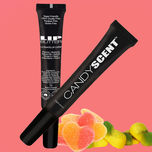 Two black tubes of lip care products are featured on a pink background. One tube, labeled "Lip Butter," highlights its vegan and cruelty-free formula with natural ingredients. Both tubes are branded with the name CANDYSCENT™. Colorful gummy heart candies are placed in the foreground, adding a playful touch.