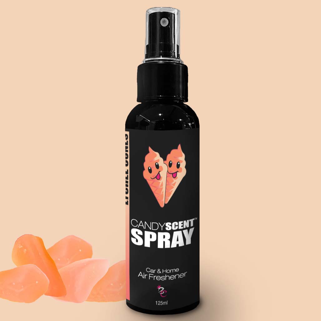 A black spray bottle labeled "CANDYSCENT™ Car & Home Scent Sprays" features an image of two ice cream cones and text indicating it is a car and home air freshener. The bottle holds 125ml. In the background, several orange gummy candies are visible on the left side. Enjoy a long-lasting fragrance with CANDYSCENT™ Car & Home Scent Sprays.