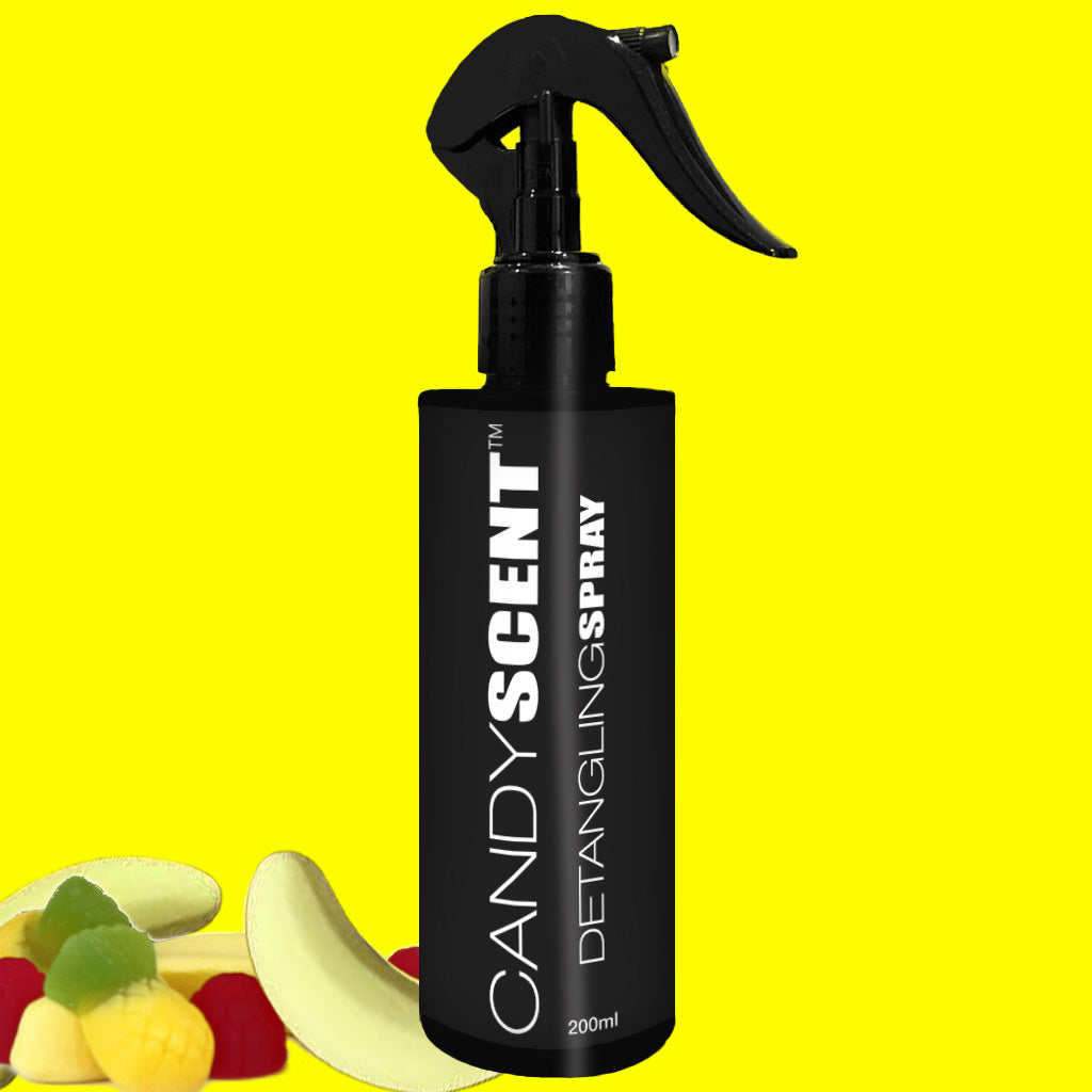 A black spray bottle labeled "CANDYSCENT™ Hair Detangling Spray 200ml" is placed against a bright yellow background. Beside the bottle are slices of colorful, fruit-shaped candies, emphasizing its delightful aroma and suitability for all hair types with the nourishing touch of Aloe Vera.