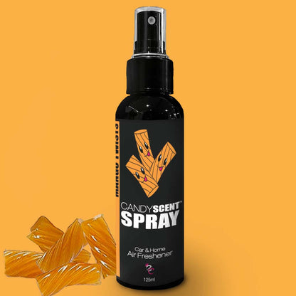 A black bottle of CANDYSCENT™ Car & Home Scent Sprays, adorned with an orange aroma design on the label, guarantees a long-lasting fragrance. The 125ml spray bottle with a nozzle sits on an orange background and is surrounded by candy pieces, effectively eliminating odors.