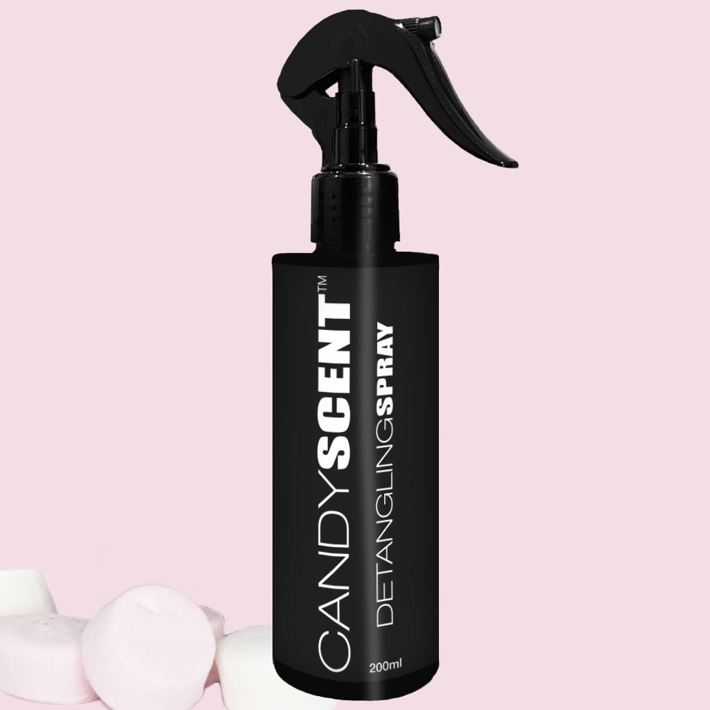 A 200ml black spray bottle labeled "CANDYSCENT™ Hair Detangling Spray" is set against a light pink background. Three pink and white marshmallows are positioned in the bottom left corner. Infused with Aloe Vera, this delightful spray is ideal for all hair types.