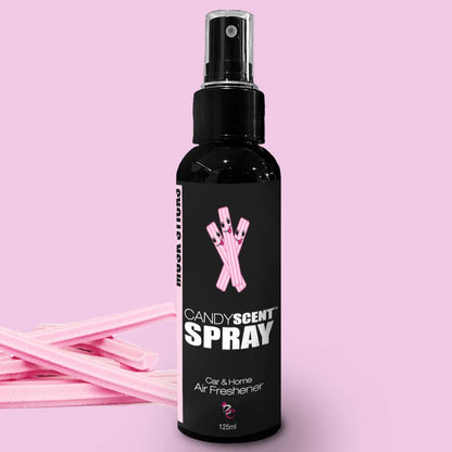 A black spray bottle labeled "Car & Home Scent Sprays by CANDYSCENT™, 125ml" is set against a light pink background. The bottle features an image of pink candy sticks, promising a long-lasting fragrance. A few candy sticks are also placed on the surface next to the bottle.