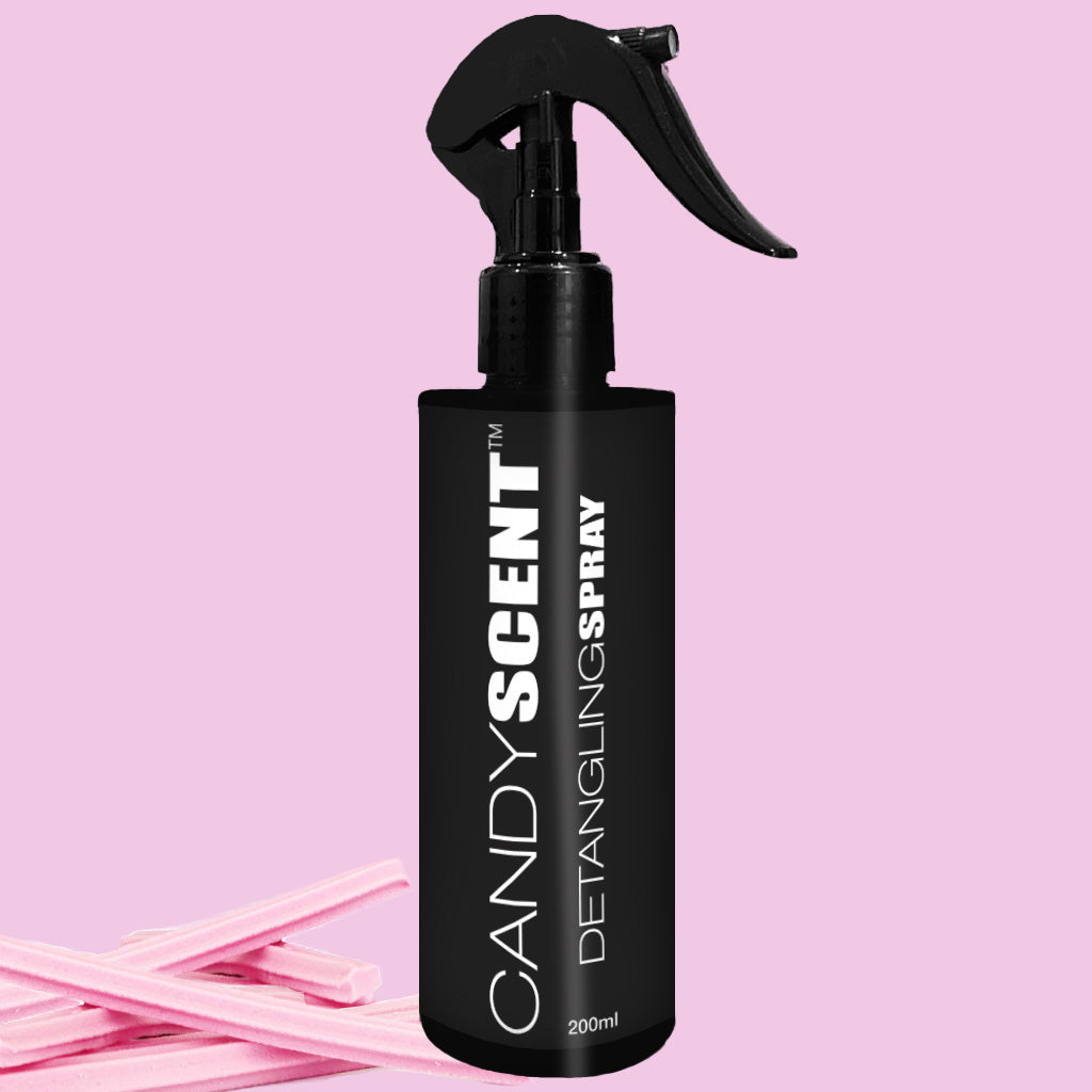 A black bottle of CANDYSCENT™ Hair Detangling Spray with a spray nozzle is showcased against a light pink background. The 200ml bottle, adorned with white text and enriched with Aloe Vera for all hair types, is complemented by pink candy sticks placed nearby, adding a playful touch to the scene.