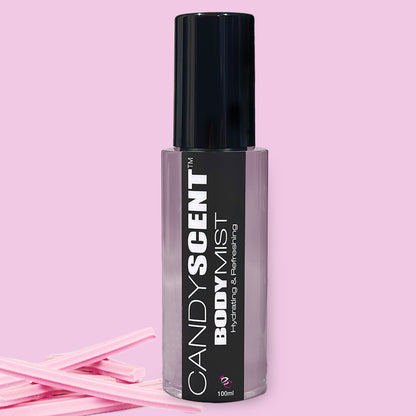 A bottle of CANDYSCENT™ Hydrating Body Mist is placed against a pink background. The sleek bottle features a black cap and a grey label with white and black text that reads "CANDYSCENT™ Hydrating Body Mist - Refreshing - 100 ml." With nourishing ingredients like witch hazel, it's surrounded by pink candy sticks at the bottom left.