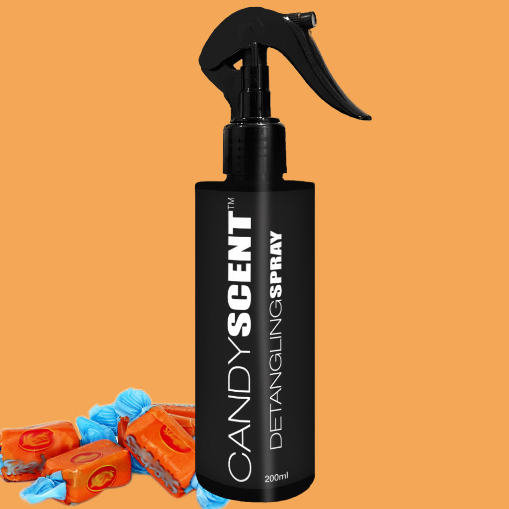 A black spray bottle labeled "CANDYSCENT™ Hair Detangling Spray" is displayed against an orange background. The 200ml bottle, suitable for all hair types, features a trigger nozzle. In the bottom left corner, a few unwrapped caramel candies with blue wrappers are partially visible.