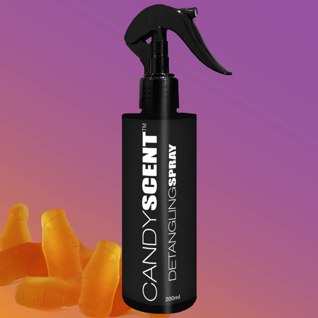 A black spray bottle labeled "CANDYSCENT™ Hair Detangling Spray 200ml" is set against a purple and orange gradient background, with orange candy corn pieces visible in the bottom left corner. Formulated with Aloe Vera, this spray is ideal for all hair types and includes a convenient trigger nozzle.