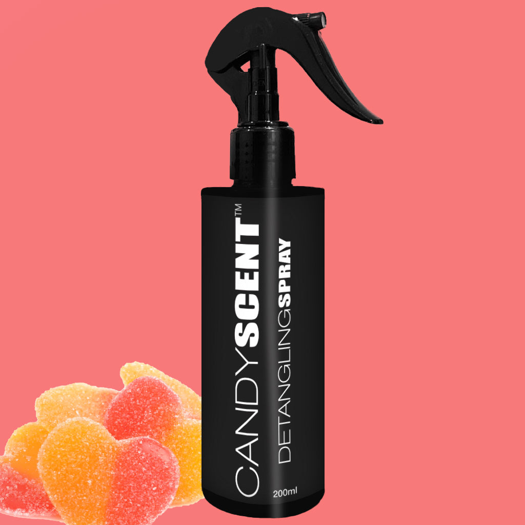 A black spray bottle labeled "CANDYSCENT™ Hair Detangling Spray" in 200ml is set against a pink background. Featuring Aloe Vera and Jojoba Oil, colorful gummy heart candies are placed at the bottom left corner of the image.