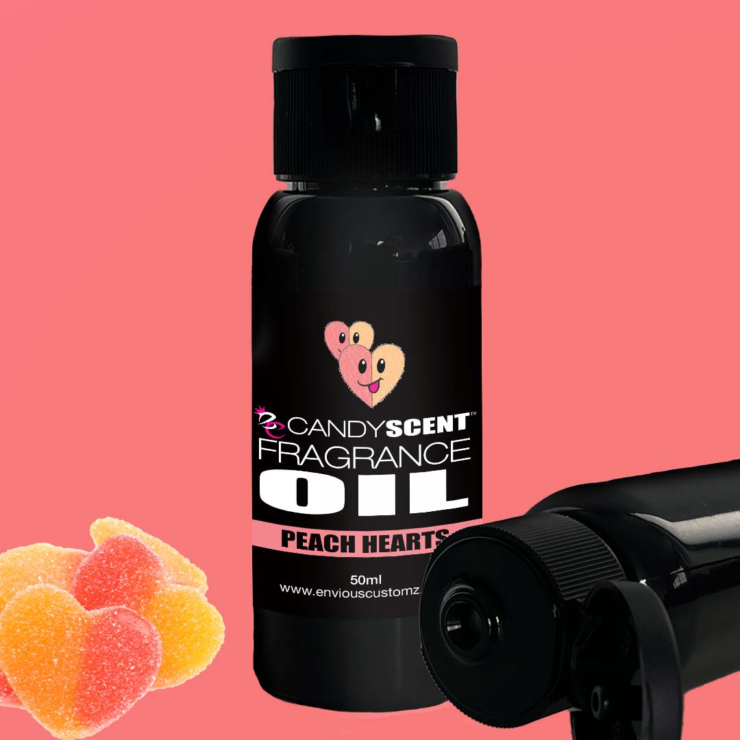 Two black bottles of CANDYSCENT™ Fragrance Oil labeled as "Peach Hearts" are set against a pink background. The labels display two heart-shaped peaches, while three heart-shaped peach gummy candies in the foreground capture the essence of this home fragrance, making it perfect for your oil burner.