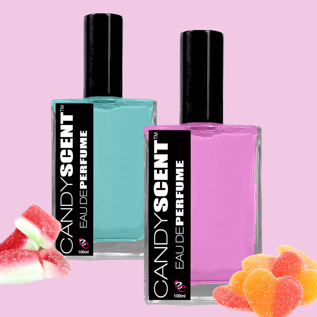 On a pink background, two rectangular perfume bottles are displayed. One bottle contains blue liquid and the other holds purple, each labeled "CANDYSCENT™ Eau De Perfume / Cologne" in black and white. Surrounding the bottles are heart-shaped gummy candies and watermelon-shaped gummies, enhancing the sweet, playful fragrances with sugary treats.