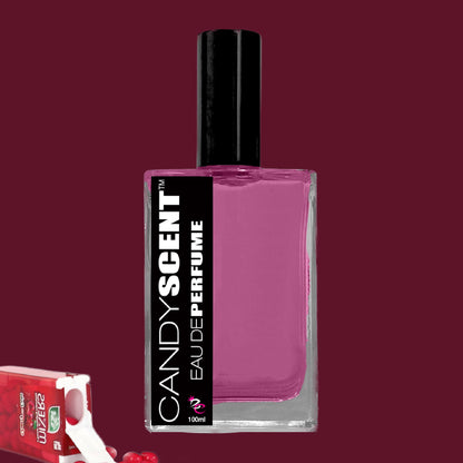 A rectangular bottle of CANDYSCENT™ Eau De Perfume / Cologne with a black cap and purple liquid inside. The black and white label details the brand and product name. A partially opened red candy wrapper with sugary treats is visible in the bottom left corner, evoking sweet playful fragrances.