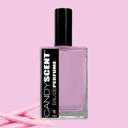 A bottle of "CANDYSCENT™ Eau De Perfume / Cologne," ideal for daily use, is displayed against a pink background. The transparent bottle reveals purple liquid inside, and the black label denotes the brand name and product type. Several pink sticks are positioned to the left of the bottle.