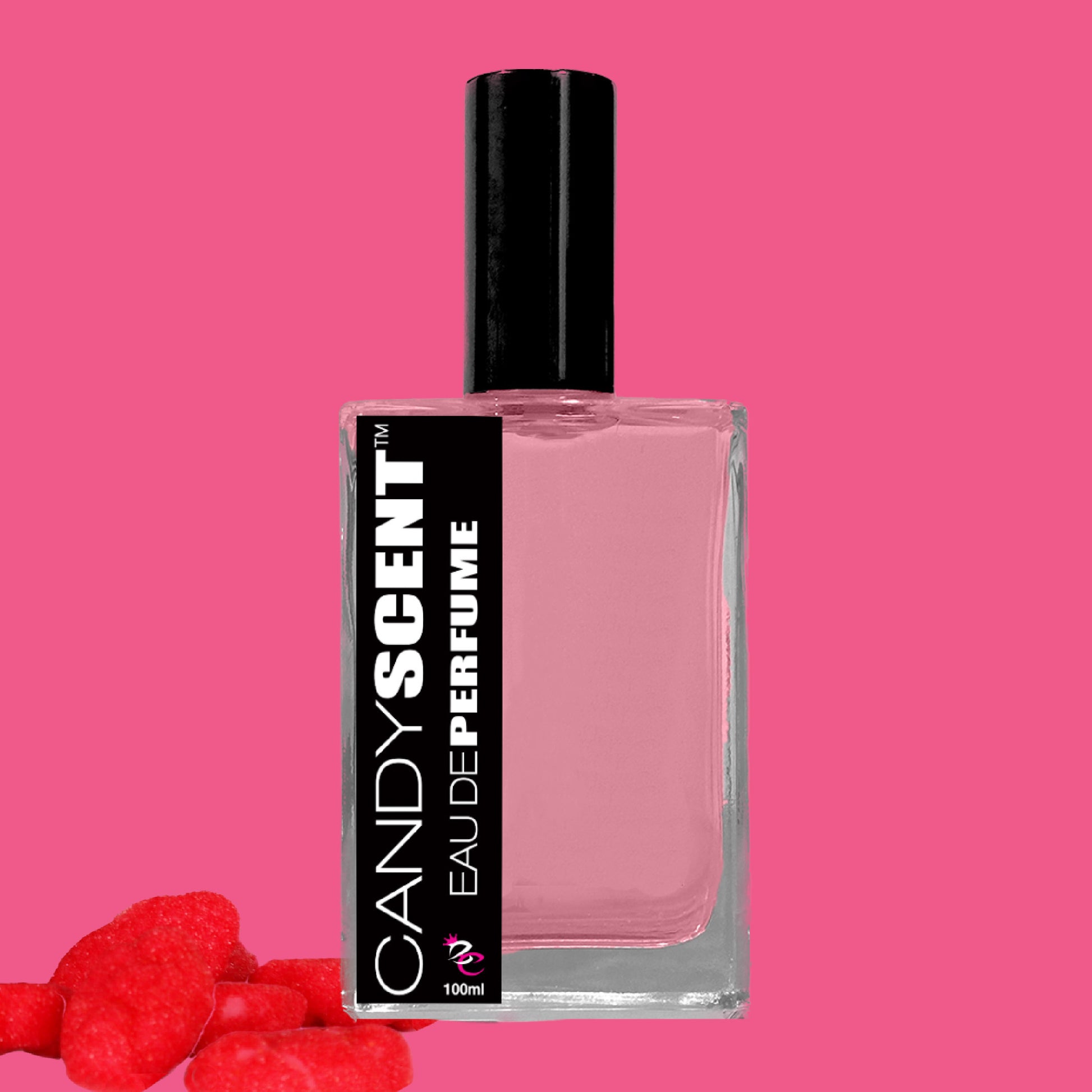 A rectangular glass bottle of CANDYSCENT™ Eau De Perfume / Cologne with pink liquid inside, a black cap, and a black label. The label reads "CANDYSCENT™ EAU DE PERFUME / COLOGNE" with a 100ml volume. In the bottom-left corner are several red candy pieces on a pink background, perfect for everyday wear and lovers of sweet fragrances.