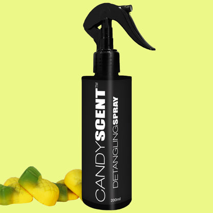 A black spray bottle labeled "CANDYSCENT™ Hair Detangling Spray" stands against a light green background. Infused with Jojoba Oil and Aloe Vera, the 200ml nozzle-topped bottle is positioned beside a few yellow and green gummy candies placed on the surface.