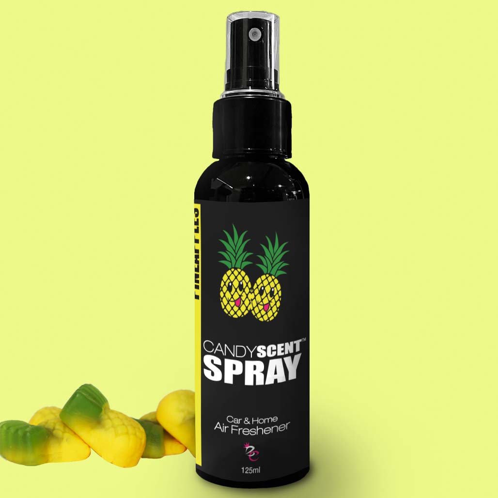 A black spray bottle labeled "CANDYSCENT™ Car & Home Scent Sprays," featuring two pineapples on its design and intended to eliminate odors in both car and home, sits against a light green background. To the left of the bottle, small yellow and green candy-shaped items enhance its long-lasting fragrance appeal.