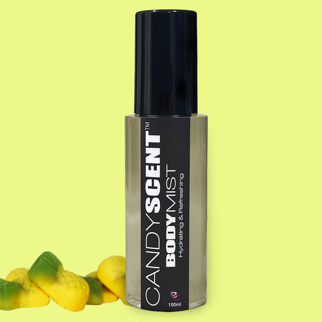 A 100ml bottle of CANDYSCENT™ Hydrating Body Mist, featuring a sleek, dark label and black cap, set against a light yellow background. The label reads "Hydrating & Refreshing" and highlights nourishing ingredients such as witch hazel. Two yellow and green gummy candies are positioned at the bottom left corner of the image.