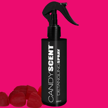 A 200ml black spray bottle of CANDYSCENT™ Hair Detangling Spray, featuring a trigger nozzle at the top, is positioned against a vibrant pink background. Infused with Jojoba Oil and Aloe Vera, it sits adjacent to several candy-shaped red gummies on the left.