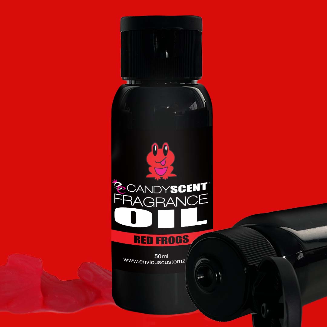 A CANDYSCENT™ Fragrance Oil bottle labeled "Red Frogs" stands upright against a red background. The black bottle showcases a red frog graphic above the label text. Two additional bottles lie on their sides, accompanied by a few red gummy candies—ideal for your home scent or oil burner needs.