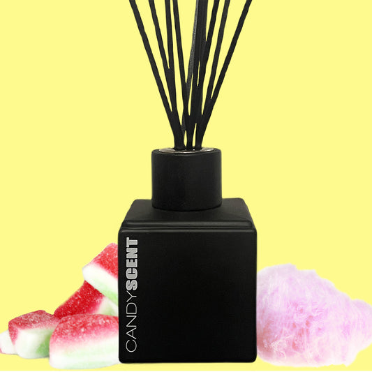 A black reed diffuser labeled "CANDYSCENT™ Reed Diffusers & Refills" is placed against a yellow background. It is surrounded by pieces of gummy watermelon candy on the left and a fluffy pink cotton candy on the right, showcasing its Australian-made, long-lasting fragrance.