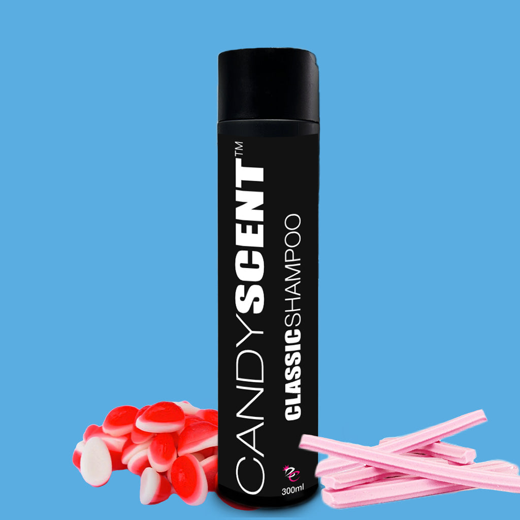 A bottle of CANDYSCENT™ Classic Shampoo in black is placed against a plain blue background. The bottle is flanked by red and white candy on the left and pink and white candy sticks on the right. The luxurious shampoo's label features white text with a small pink logo at the bottom, epitomizing premium hair care.