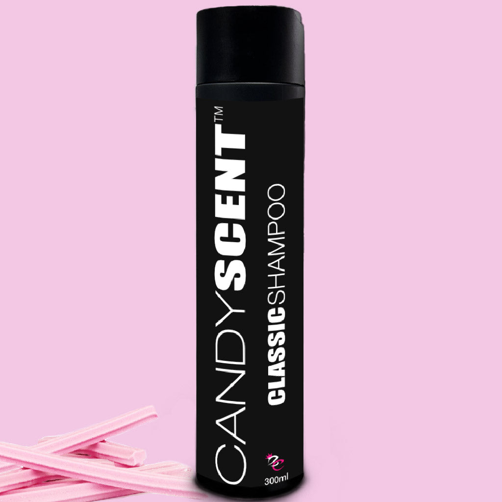 A black bottle of CANDYSCENT™ Classic Shampoo with white text stands upright against a pink background. This luxurious 300ml shampoo epitomizes premium hair care. Two pieces of candy are placed at the base of the bottle for a sweet touch.