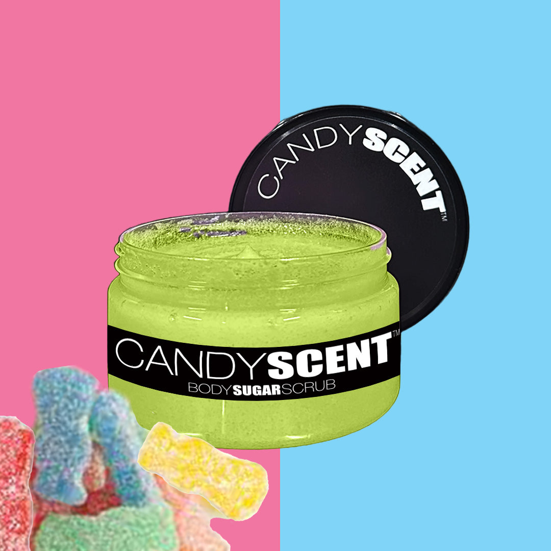 A jar of CANDYSCENT™ Body Sugar Scrub, enriched with exfoliating and hydrating properties, showcases a lime-green scrub substance. With its lid set beside it on a split pink and blue background, the display is enhanced by assorted colorful gummy candies in the lower left corner.