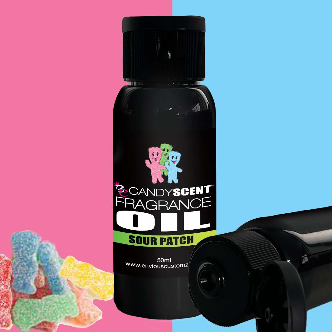 A black bottle labeled "CANDYSCENT™ Fragrance Oil" in the scent "Sour Patch" is showcased against a split pink and blue background. Sour candy pieces are visible to the left. Another partially visible black bottle lies horizontally, parallel to the main bottle—ideal for your oil burner or home scent collection.