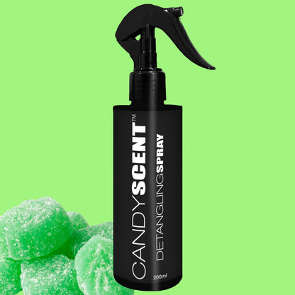 A black bottle of CANDYSCENT™ Hair Detangling Spray, featuring a spray nozzle, is set against a vibrant green backdrop. Green, sugar-coated candy pieces in the lower left corner enhance the scene with their sweetness. This 200ml bottle, enriched with Aloe Vera, promises to work wonders on all hair types.