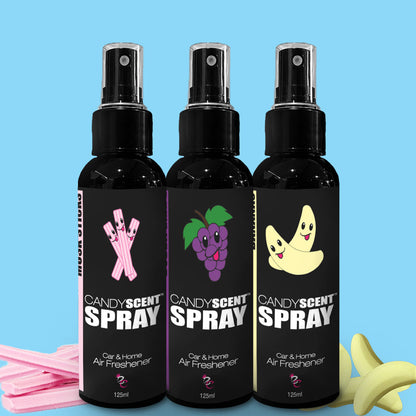 Three bottles of CANDYSCENT™ Car & Home Scent Sprays are lined up against a blue background, with each scent labeled as strawberry, grape, and banana. Each bottle is illustrated with corresponding fruit images to represent the scent. Featuring long-lasting fragrances that eliminate odors, the display also includes pink gum strips and banana-shaped candies at the bottom.