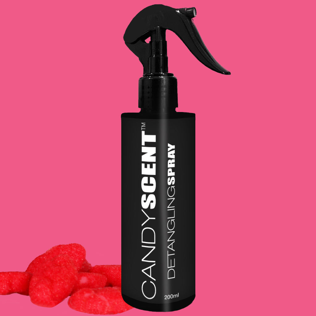 A black 200ml bottle labeled "Hair Detangling Spray" by CANDYSCENT™ with a spray nozzle sits against a bright pink background. Red candy-like objects are placed at the base of the bottle. Infused with Aloe Vera, it's perfect for all hair types.