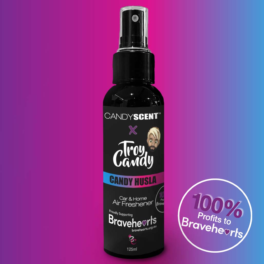 A black 125ml spray bottle of CANDYSCENT™ x Troy Candy Car Spray by CANDYSCENT™ against a gradient purple and blue background. The label highlights that 100% of profits go to the Bravehearts foundation, featuring a prominent charity logo and a cartoon character graphic.