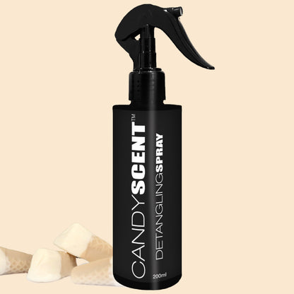 A black bottle labeled "CANDYSCENT™ Hair Detangling Spray" with a trigger spray top is centered in the image. The 200ml bottle features Aloe Vera and Jojoba Oil for added nourishment. In the bottom left corner, three small pieces of white candy lie against a beige background.