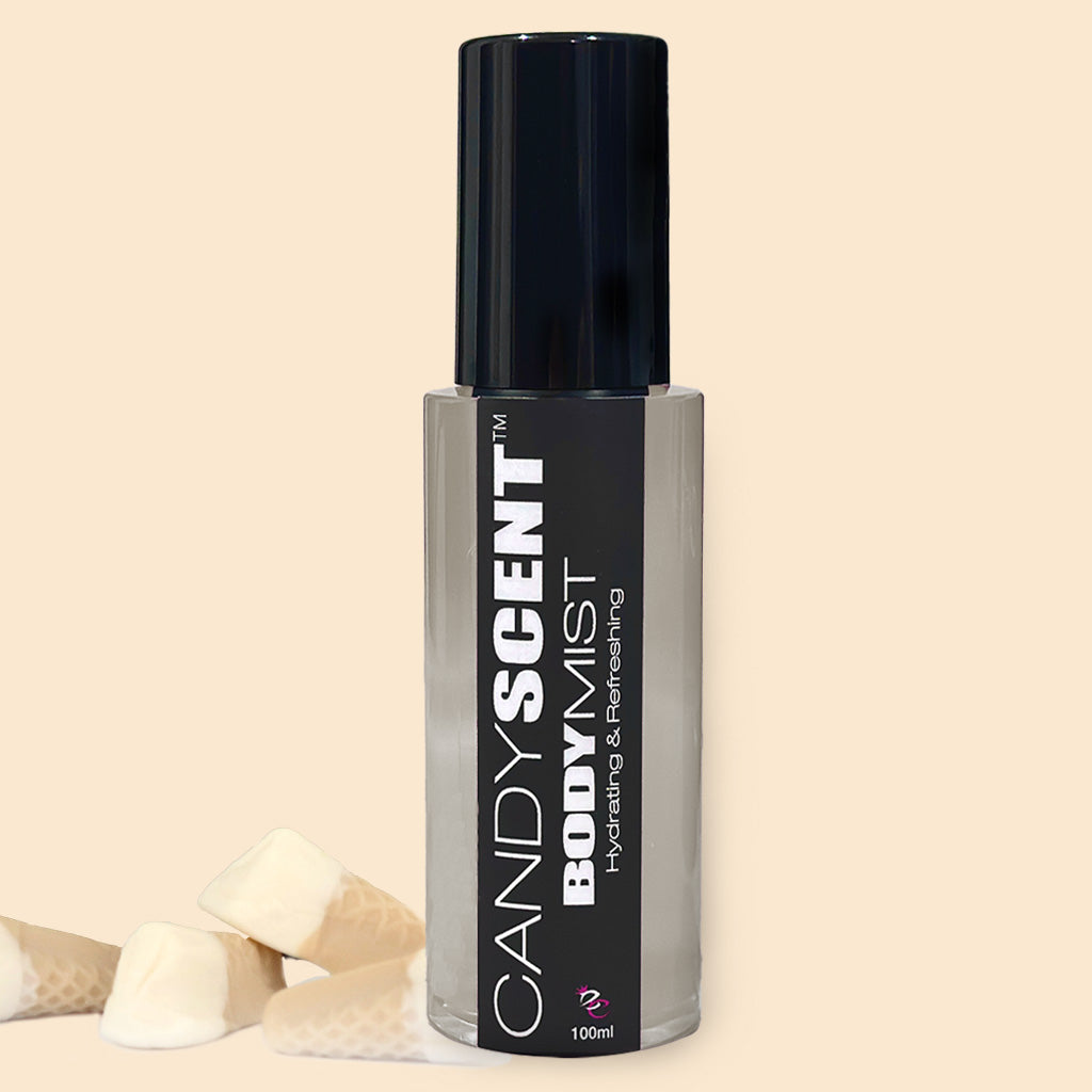 A transparent bottle of CANDYSCENT™ Hydrating Body Mist with a black cap and label stands against a light beige background. The label reads "CANDYSCENT™ Hydrating Body Mist - Hydrating & Refreshing, infused with Witch Hazel." Nearby, a few pieces of white candy with a waffle-like texture are displayed.