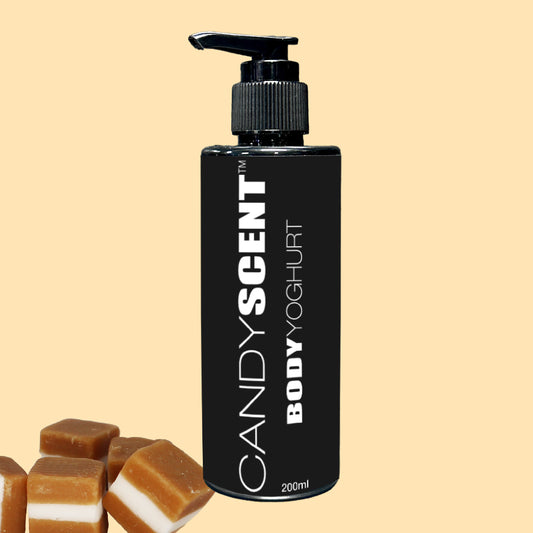 A black bottle with a pump dispenser, labeled "Body Yoghurt" by CANDYSCENT™, sits against a beige background, offering deep hydration. To the left, caramel-colored candies are stacked in the corner, enhancing the nourishing experience.