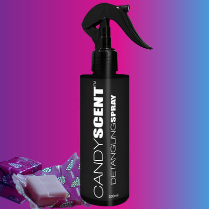 A black spray bottle labeled "CANDYSCENT™ Hair Detangling Spray" stands upright with a trigger nozzle, set against a gradient pink and blue background. To the left of the bottle, there are two wrapped candies and a soap bar. Infused with Aloe Vera and Jojoba Oil, this detangling spray is perfect for all hair types.