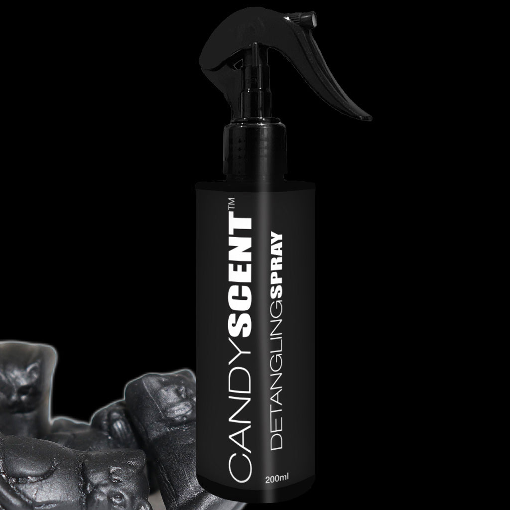 A black spray bottle labeled "CANDYSCENT™ Hair Detangling Spray" sits against a dark background. The 200 ml bottle, equipped with a pump nozzle, is enriched with nourishing Jojoba Oil. The backdrop features an indistinct, blurred dark object.